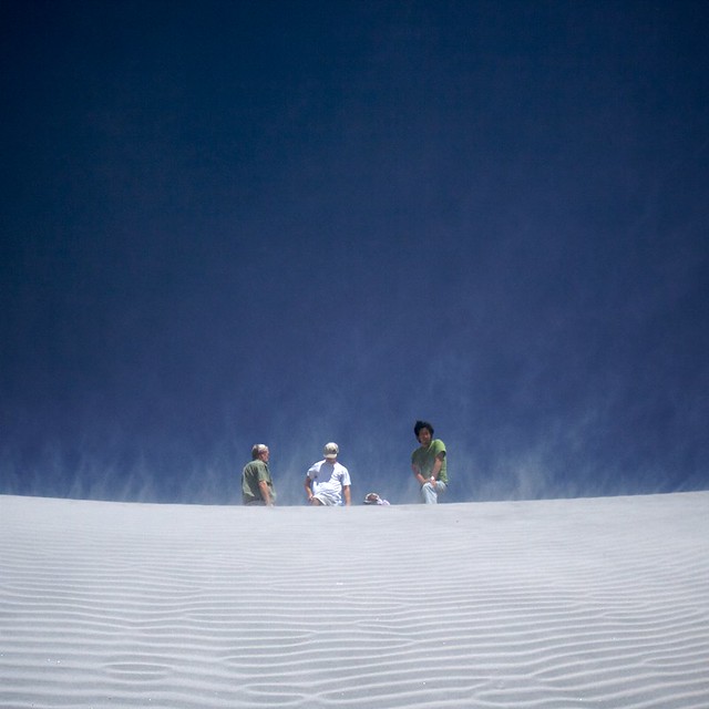 Three scientists stand atop a barchan dune on a windy day.